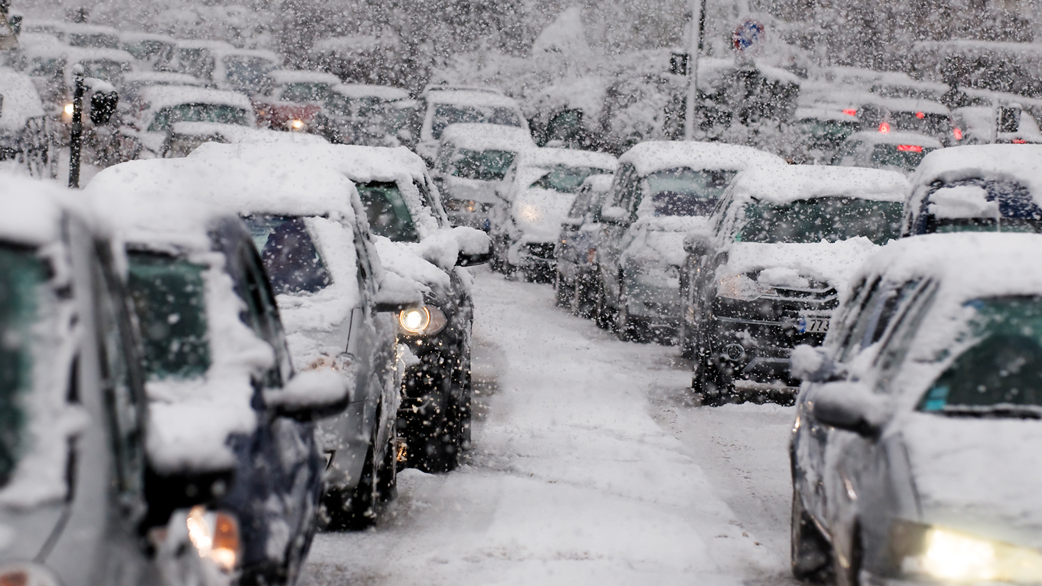 Des files de voitures, couvertes de neige, attendent sur des routes enneigées.